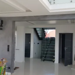 Wnętrze domu w Słubicach po remoncie, z widoczną szarą ścianą o nieregularnej fakturze, jasną podłogą z połyskiem, szklanymi schodami i drzwiami w kolorze antracytowym.