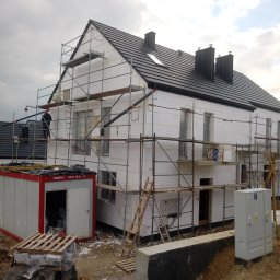 Swistak BUD - Dom w trakcie ocieplania styropianem, widoczne rusztowania, kontener budowlany i materiały izolacyjne na paletach.