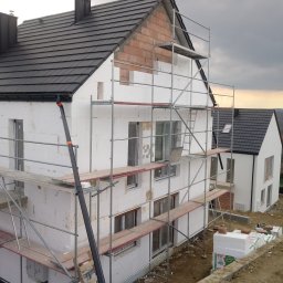 Swistak BUD - Dom w trakcie ocieplania styropianem, widoczne rusztowania, niezakończona elewacja i fragmenty muru z cegły, obok drugi dom z gotową elewacją.