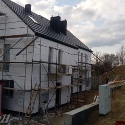 Swistak BUD - Dom w trakcie ocieplania styropianem, widoczne rusztowania, czarna dachówka i skrzynki gazowe na ścianie.