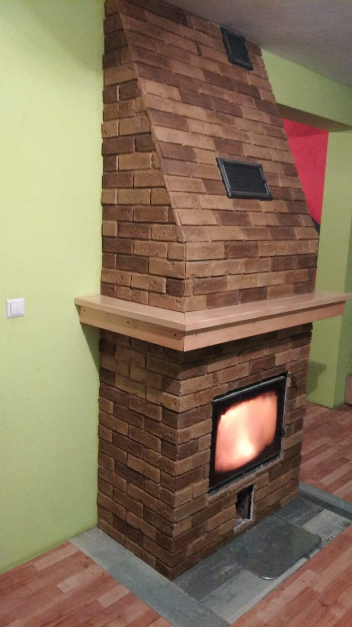 Wykończony kominek z cegły wewnątrz pomieszczenia z drewnianą półką i palącym się ogniem.