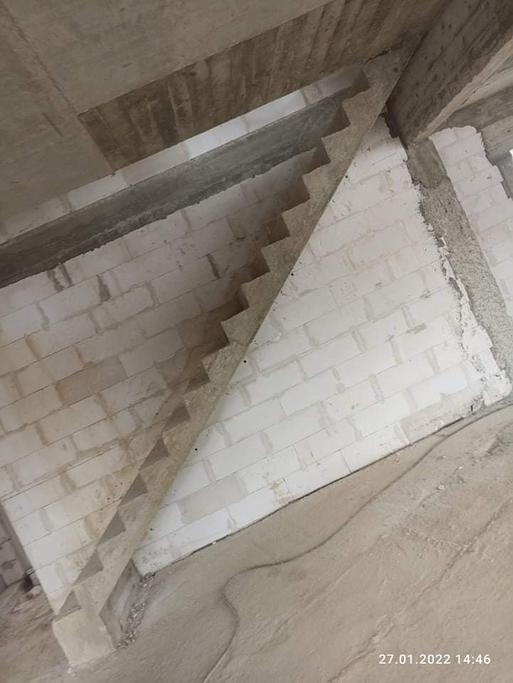 Surowe, betonowe schody w trakcie budowy wewnątrz budynku z białych bloczków, widoczne elementy konstrukcyjne sufitu, podłoga wylewka betonowa.