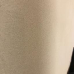 Tynki Maszynowe - Niedoskonała powierzchnia ściany w Nowym Tomyślu, z widocznymi drobnymi nierównościami i niedociągnięciami, słabe oświetlenie.