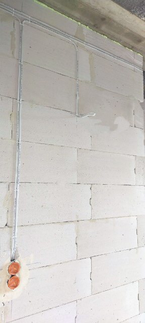 Instalacja elektryczna w korytkach na ścianie z betonu komórkowego, widoczne puszki instalacyjne i przewody.