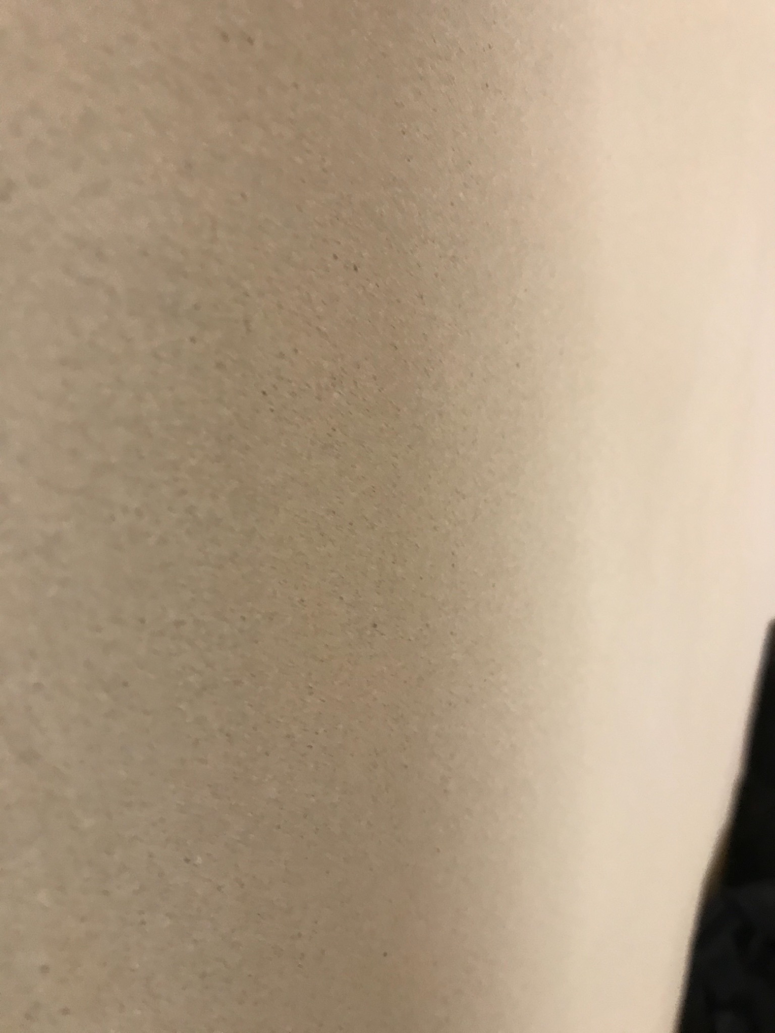 Niedoskonała powierzchnia ściany w Nowym Tomyślu, z widocznymi drobnymi nierównościami i niedociągnięciami, słabe oświetlenie.