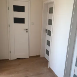 Dwa białe, nowoczesne drzwi wewnętrzne z przeszkleniami w nowym mieszkaniu z panelami podłogowymi w kolorze drewna.