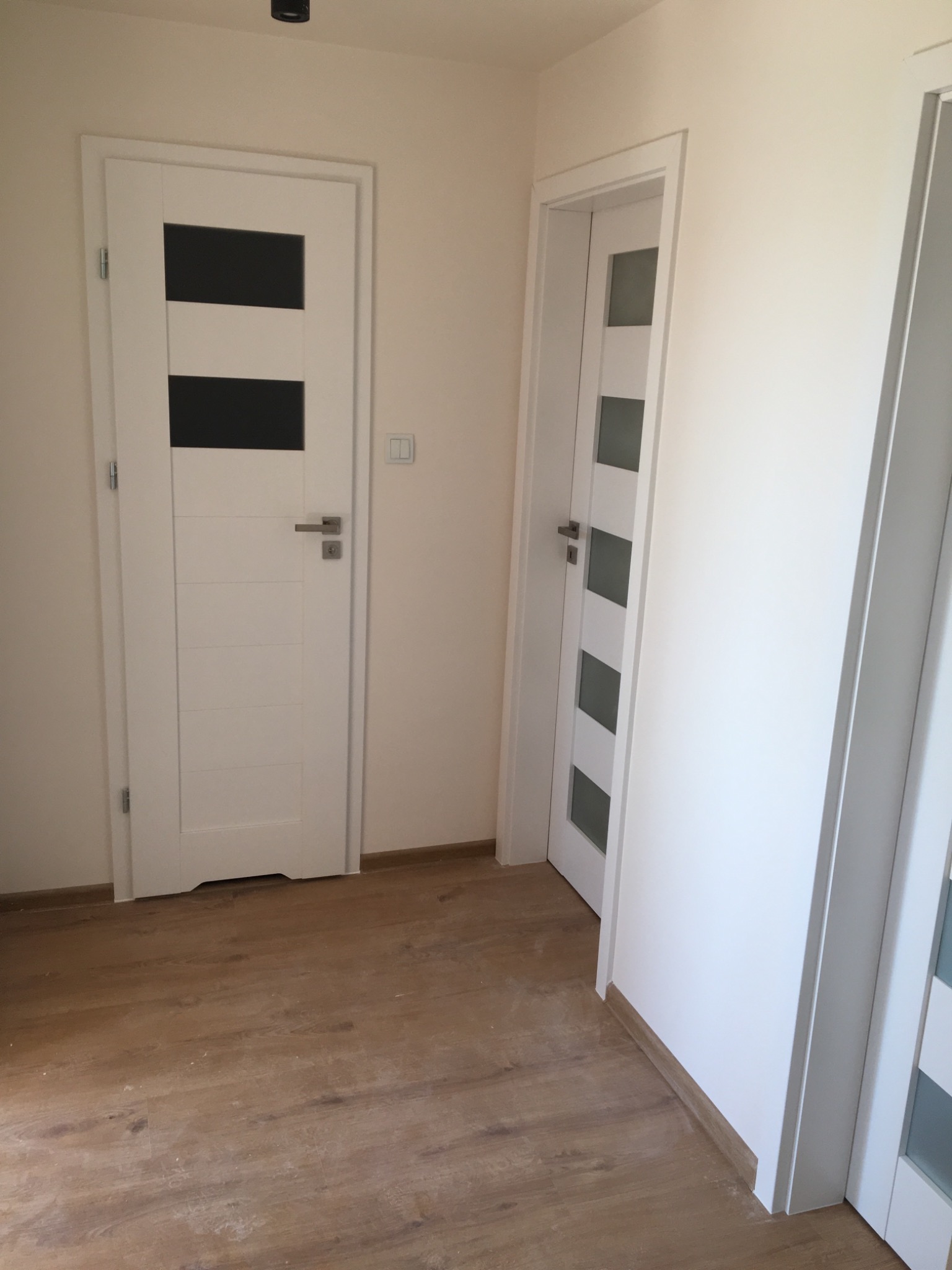 Dwa białe, nowoczesne drzwi wewnętrzne z przeszkleniami w nowym mieszkaniu z panelami podłogowymi w kolorze drewna.