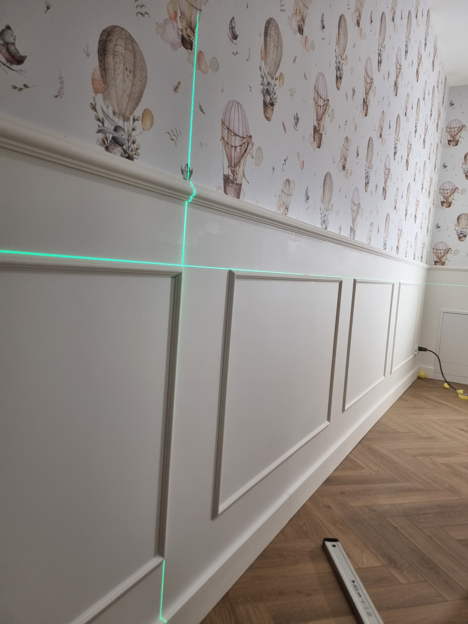 Biała boazeria angielska na ścianie z tapetą w balony, wyznaczana laserowo. Parkiet w jodełkę na podłodze. Listwa przypodłogowa.