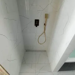 Kabina prysznicowa z białymi płytkami imitującymi marmur, złotą armaturą i odpływem liniowym.