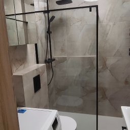 FachGro usługi remontowe - Wykończona łazienka z kabiną typu walk-in, płytkami imitującymi marmur, czarną armaturą i pralką Samsung. Nowoczesny design, oświetlenie sufitowe.