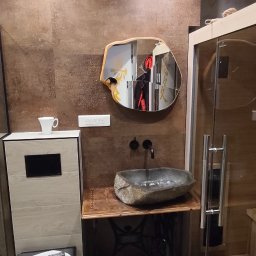 FachGro usługi remontowe - Nowoczesna łazienka z umywalką z kamienia na podstawie maszyny do szycia Singer, lustro w drewnianej ramie o nieregularnym kształcie, brązowe płytki na ścianach.