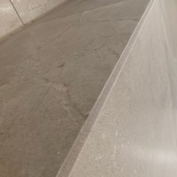FachGro usługi remontowe - Beżowa, marmurkowa płytka ścienna w łazience, ułożona z precyzją, z widoczną krawędzią i fugą. Minimalistyczny design, ciepłe oświetlenie.