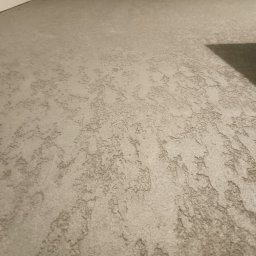 FachGro usługi remontowe - Szara, teksturowana powierzchnia ściany z widocznym cieniem w prawym górnym rogu, ukazująca unikalną strukturę i wykończenie gładzi dekoracyjnej.