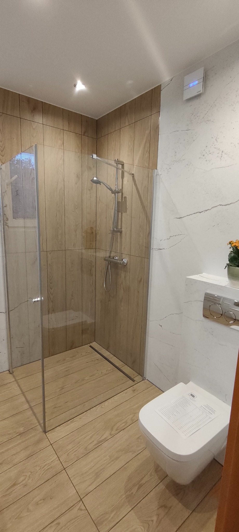 Nowoczesna kabina prysznicowa typu walk-in z drewnopodobnymi płytkami w Wolicach. Biała armatura i marmurowe ściany tworzą elegancki kontrast.