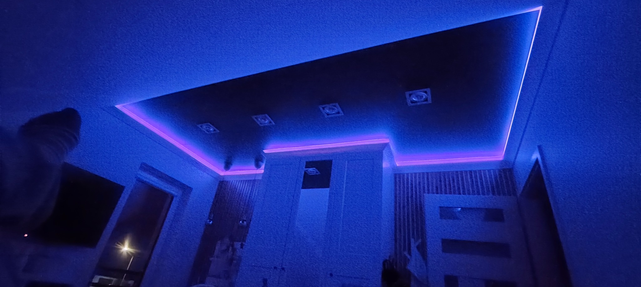 Podwieszany sufit z oświetleniem LED w kolorze fioletowym i niebieskim. Cztery kwadratowe lampy w suficie. Widok z dołu, wnętrze w chłodnej tonacji.