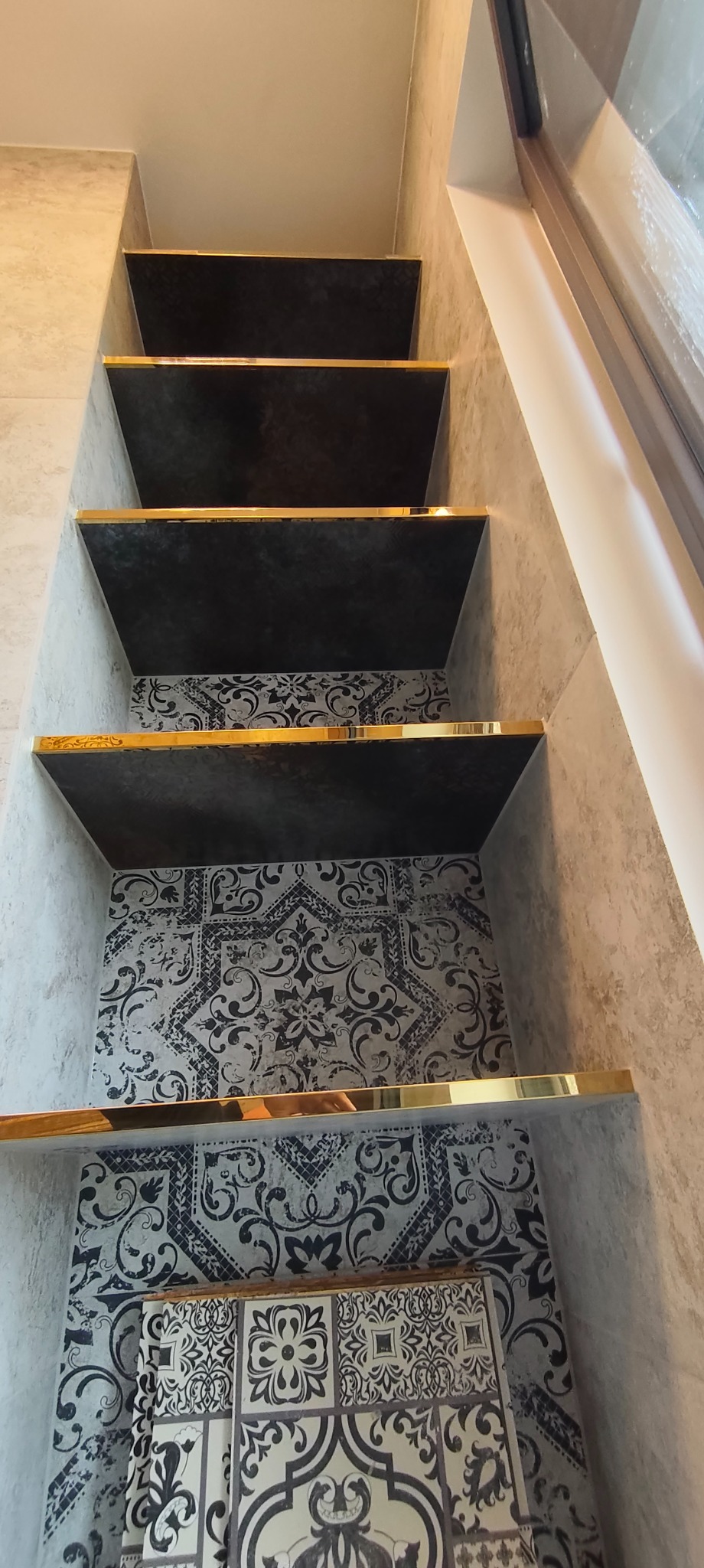 Nietypowe półki wnękowe w łazience, wykończone płytkami w czarno-białe wzory i złotymi listwami. Ujęcie z dołu, podkreślające pionowy układ.