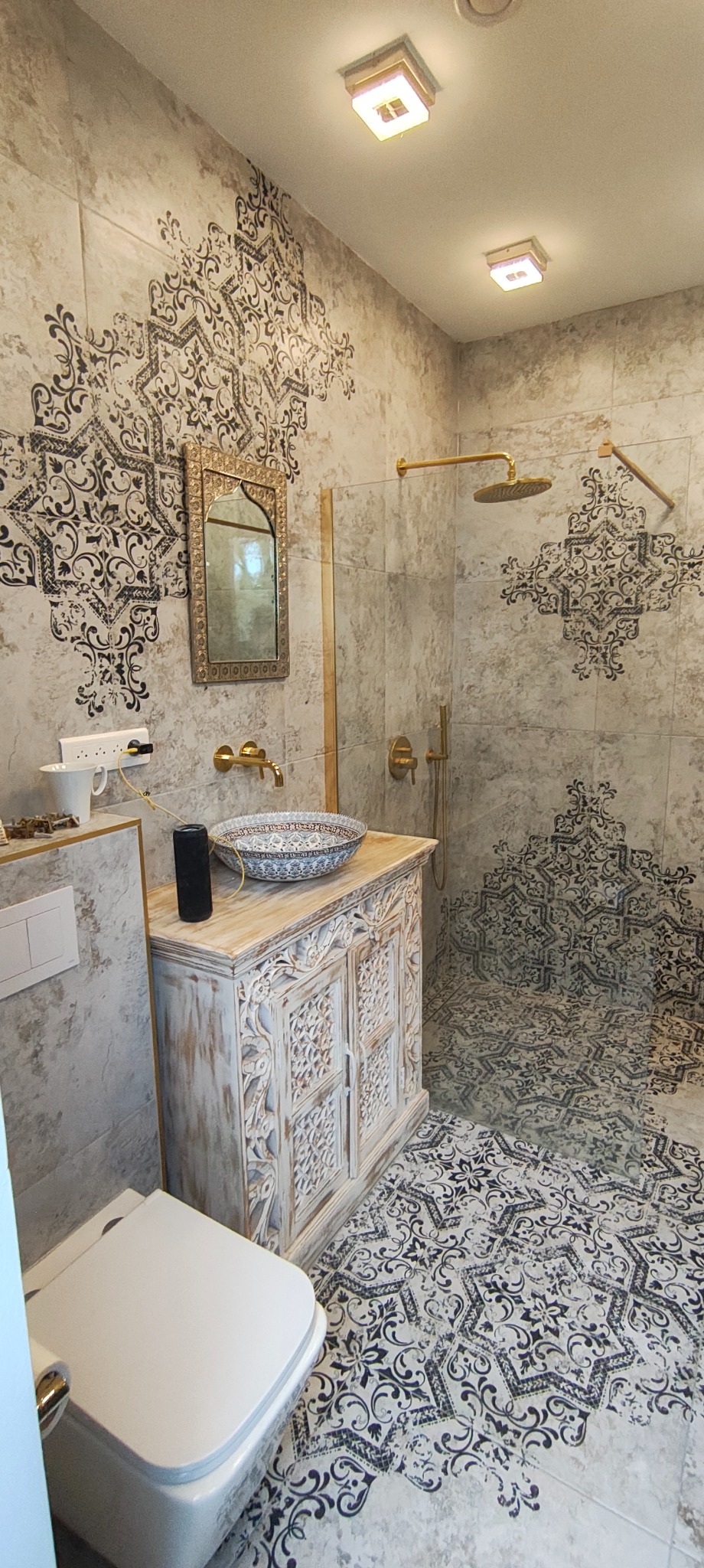Wykończona łazienka w stylu marokańskim: wzorzyste płytki, drewniana szafka pod umywalką z misą, złota armatura, lustro w ozdobnej ramie i kabina prysznicowa.