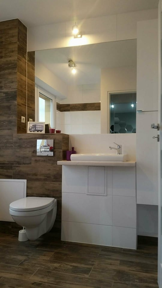 Nowoczesna łazienka w Białymstoku z brązowymi płytkami imitującymi drewno na podłodze i ścianach, biała ceramika sanitarna, umywalka nablatowa i duże lustro na ścianie.