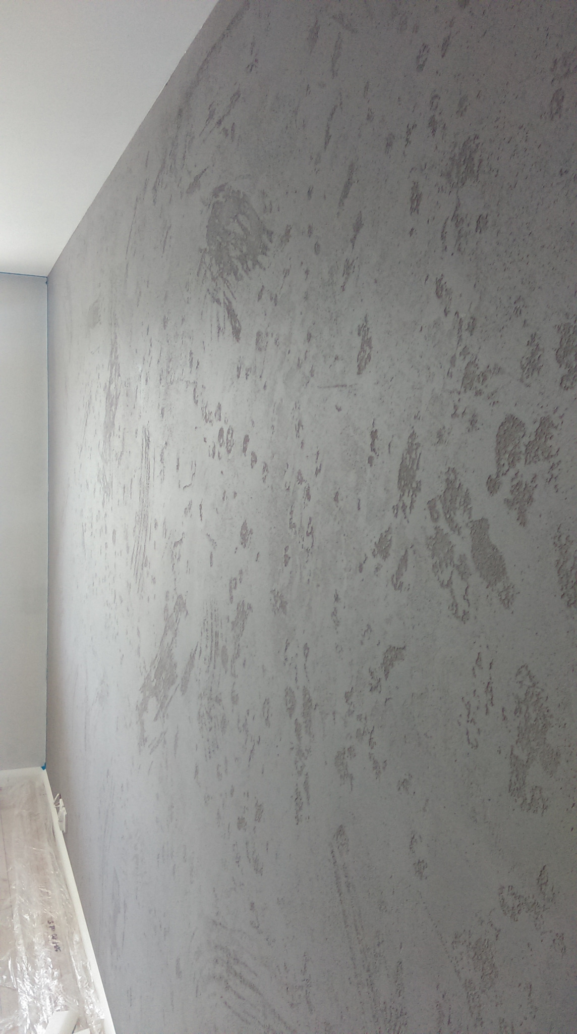 Ściana w pokoju pokryta szarą, dekoracyjną farbą strukturalną. Podłoga zabezpieczona folią malarską.