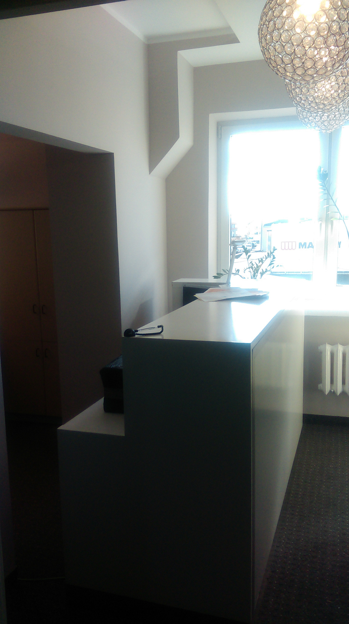 Nowoczesne, minimalistyczne biuro z białą recepcją, widoczne kryształowe lampy sufitowe i okno z rośliną doniczkową, ujęcie z niskiego kąta.