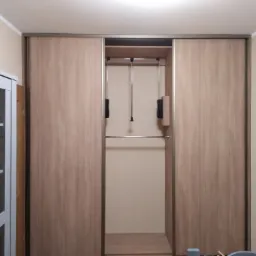 Wnętrze szafy przesuwnej z drążkiem i wysuwanymi wieszakami, widoczna z boku biała witryna z półkami.