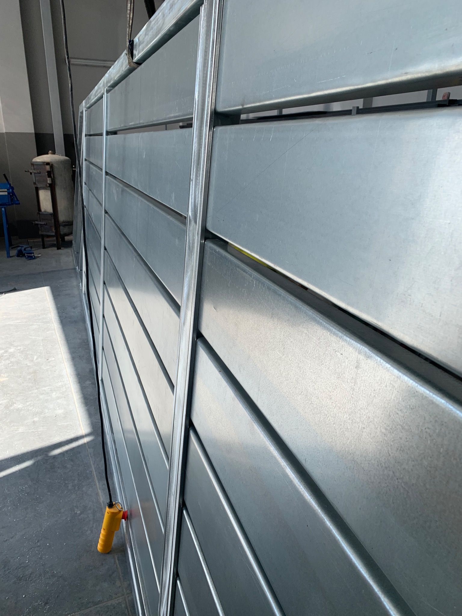 Szara brama z poziomych profili stalowych, widoczny element sterujący podnoszeniem bramy.