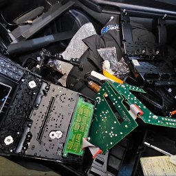 InterSatNet - Rozłożony panel sterowania z elementami elektroniki, w tym zielone płytki drukowane i białe moduły, leżące na czarnym, teksturowanym tle, prawdopodobnie w samochodzie.