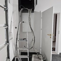 InterSatNet - Montaż szafy serwerowej w garażu: widok na drabinkę, przewody i częściowo otwarte drzwi, ukazujący etap prac instalacyjnych w surowym wnętrzu.