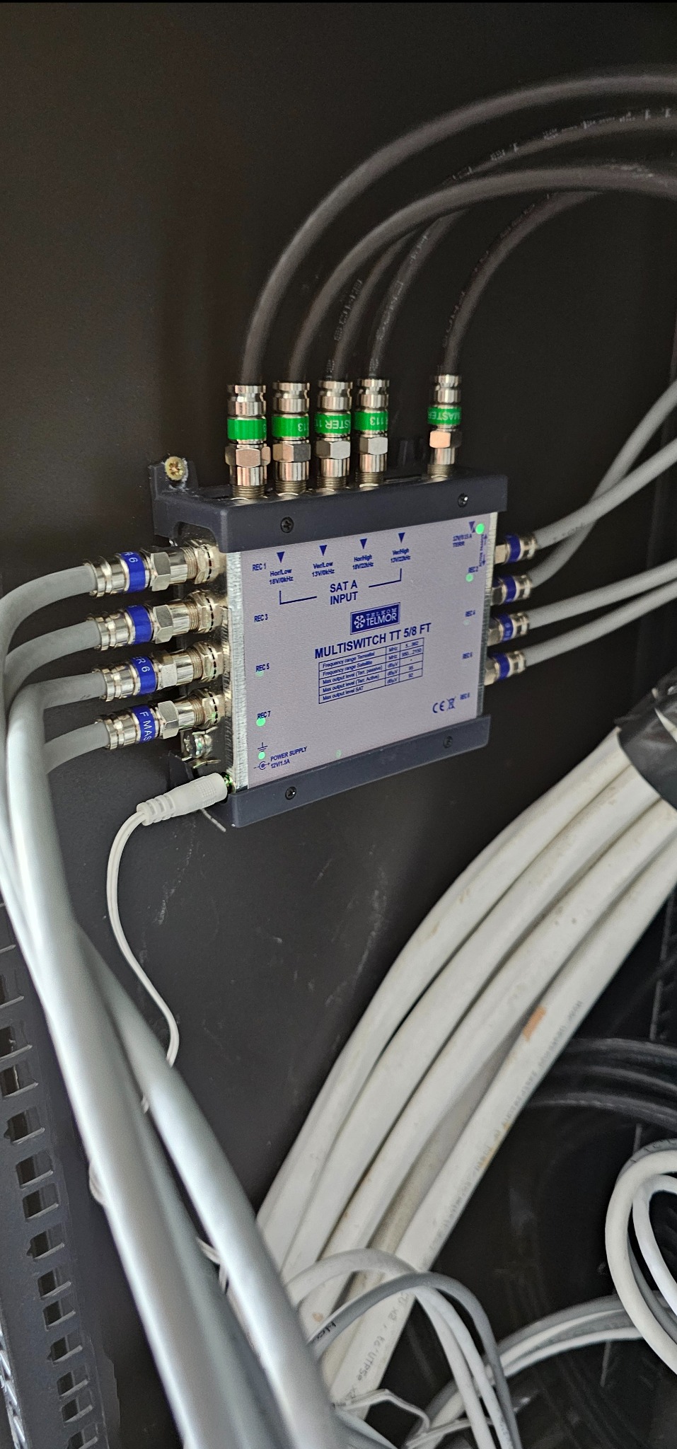 Multiswitch Telmor TT 5/8 FT z podłączonymi kablami koncentrycznymi w kolorach czarnym i szarym, zamontowany na czarnej powierzchni.