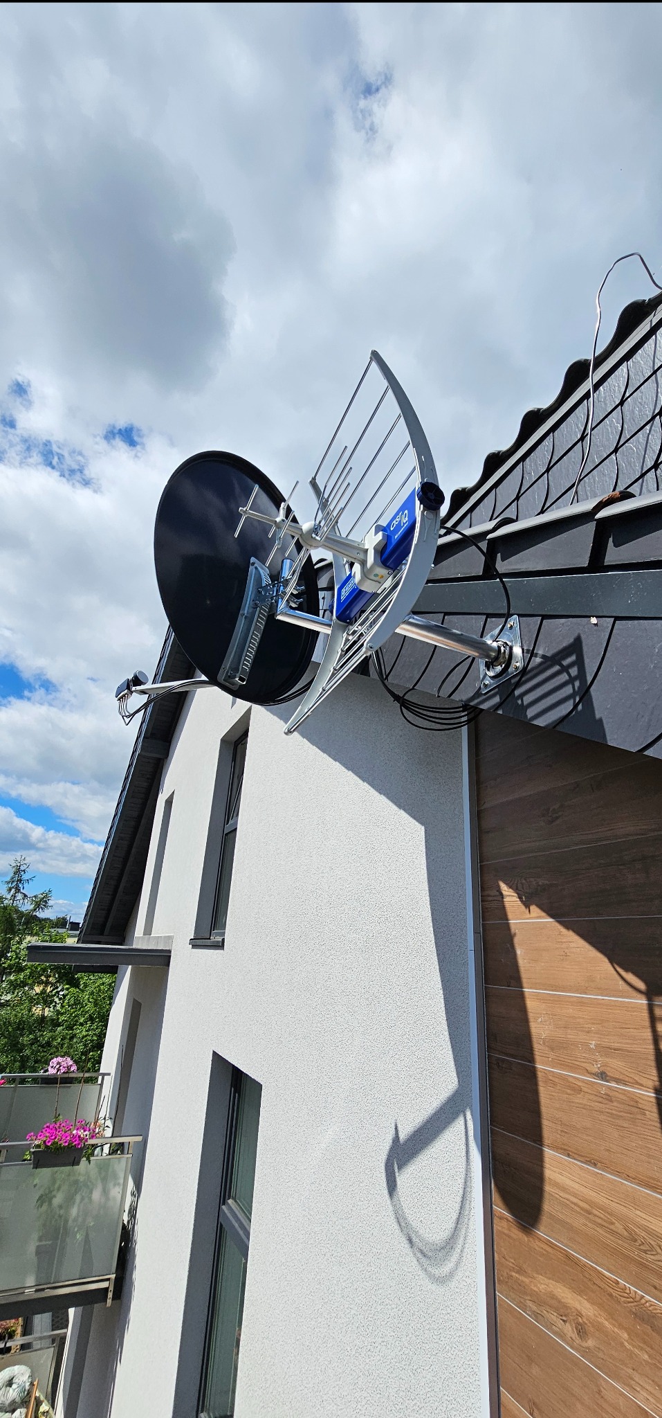 Antena satelitarna i kierunkowa zamontowana na dachu domu jednorodzinnego. Widoczne kable, mocowania i fragment elewacji budynku z oknami.