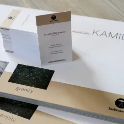 Stos wizytówek firmy Jaskiniowiec na tle wzornika kamieni naturalnych z próbkami granitu i marmuru.
