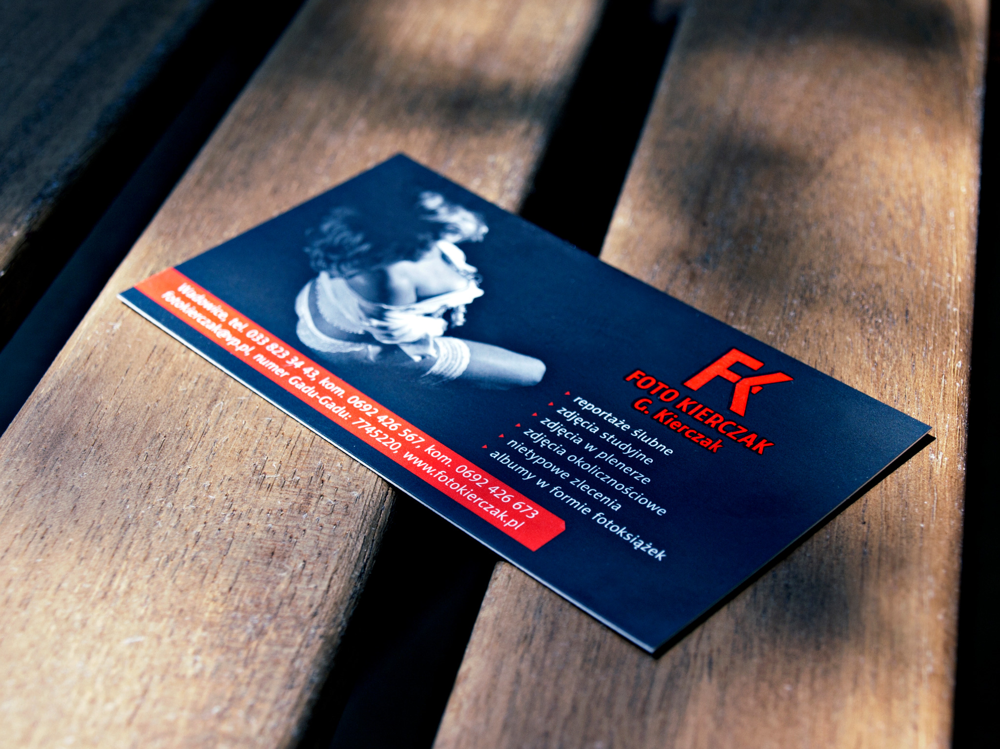 Wizytówka fotografa na drewnianym tle, prezentująca ofertę reportaży ślubnych, zdjęć studyjnych i plenerowych, albumów okolicznościowych i nietypowych zleceń.