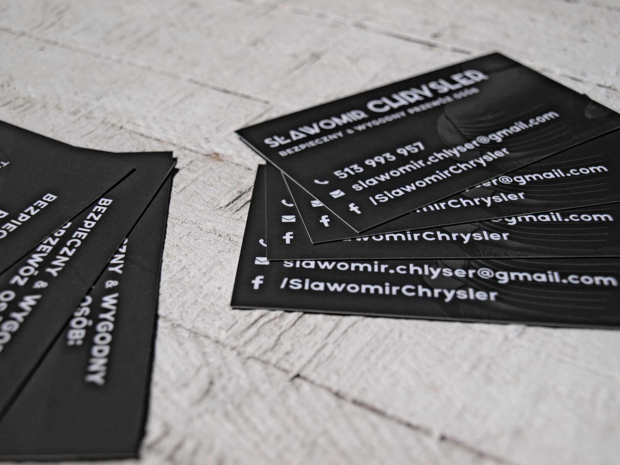 Stos czarnych wizytówek z białym tekstem na jasnym, drewnianym tle, prezentujący dane kontaktowe firmy Sławomir Clydsler.