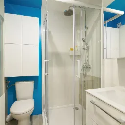 Jasna łazienka z kabiną prysznicową, umywalką z szafką, toaletą i niebieską ścianą akcentującą.