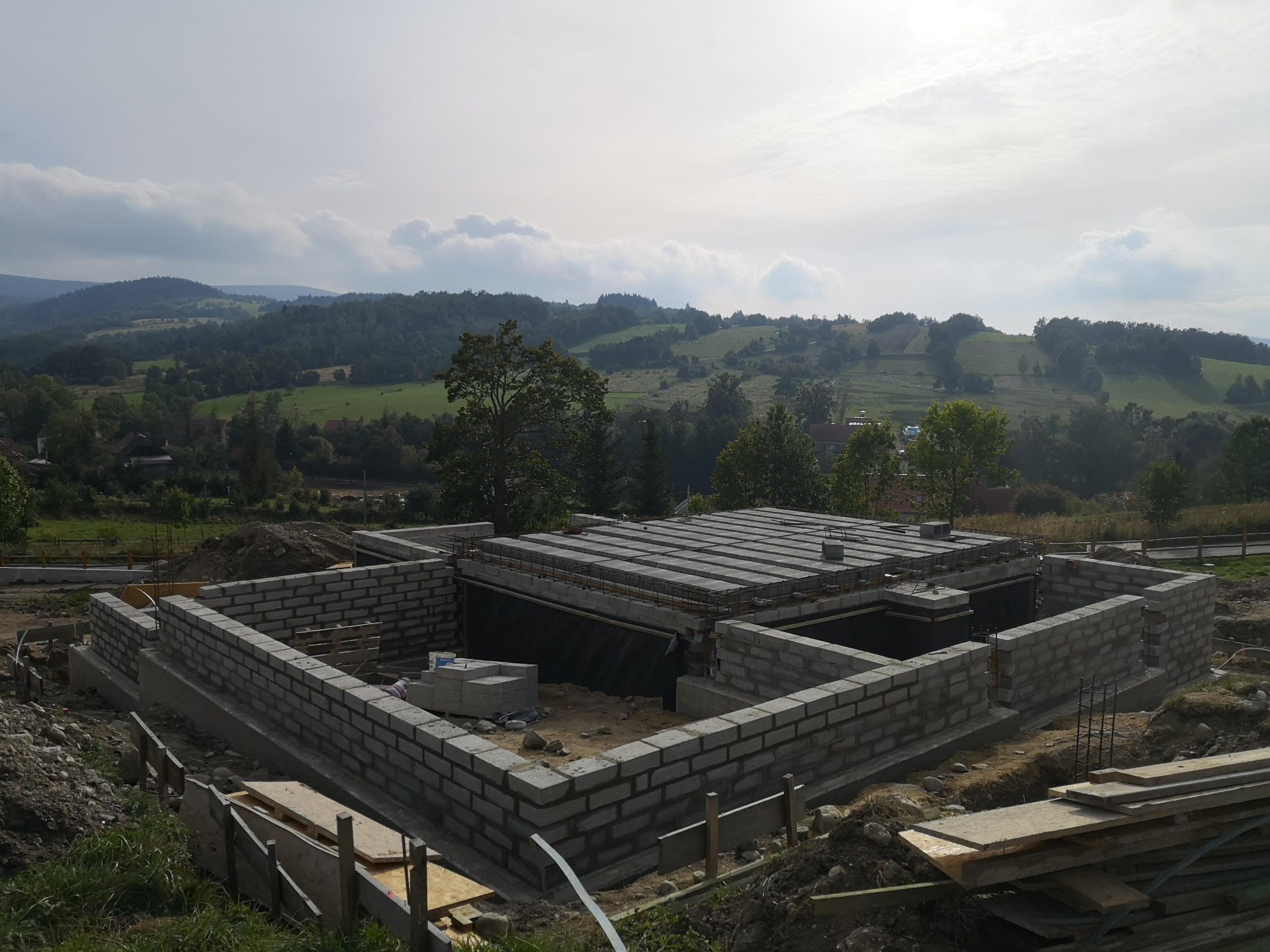 Budowa domu w toku: wzniesione ściany fundamentowe z bloczków betonowych na tle malowniczego krajobrazu pagórkowatego.