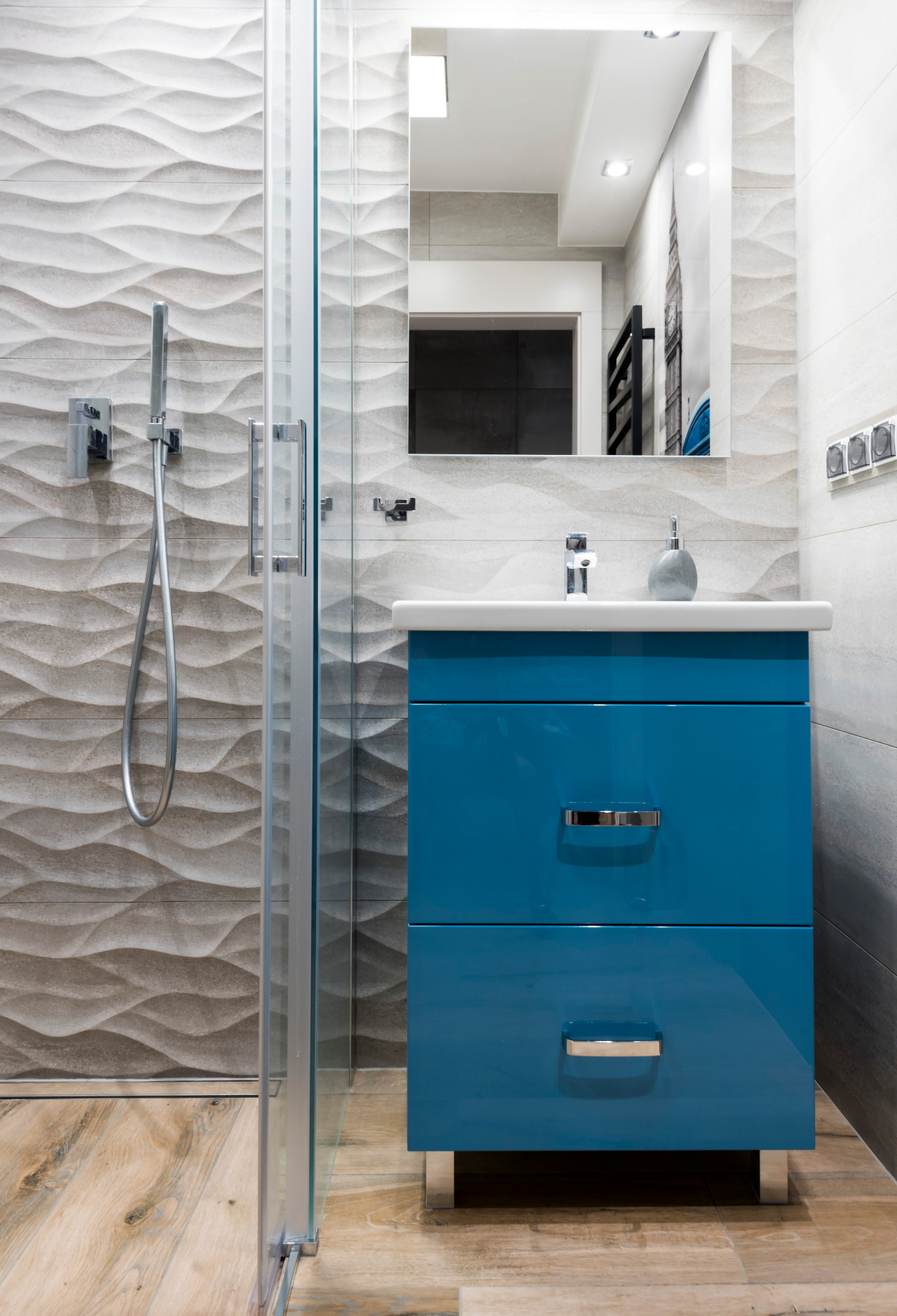 Nowoczesna łazienka z kabiną prysznicową, umywalką na szafce w odcieniu błękitu i lustrem, gdzie w odbiciu widoczny jest motyw Big Bena.