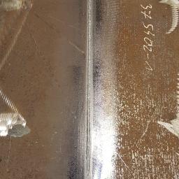 Jaśkiewicz Constructions - Spoina spawalnicza łącząca dwie metalowe płyty, widoczne ślady po szlifowaniu i oznaczenia na powierzchni.