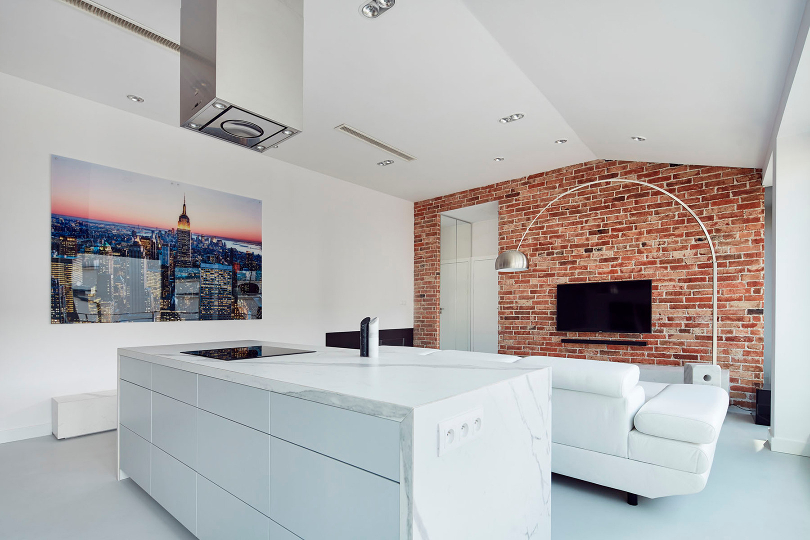 Nowoczesna kuchnia z wyspą wykończoną marmurem, na ścianie duży obraz z panoramą Nowego Jorku, ściana z czerwonej cegły w tle.