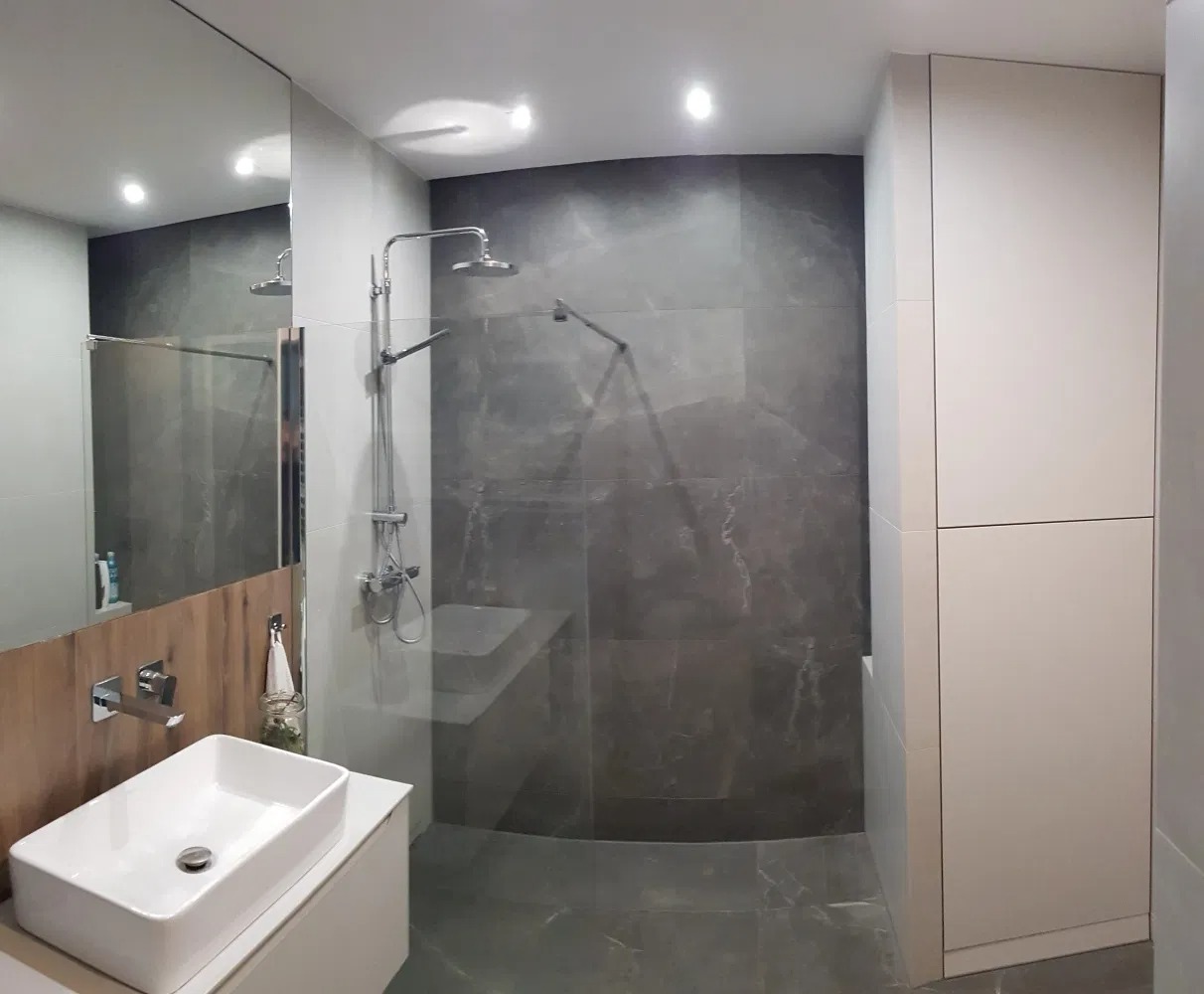 Nowoczesna łazienka z szarymi płytkami imitującymi marmur, białą umywalką nablatową i kabiną prysznicową typu walk-in z chromowaną armaturą.