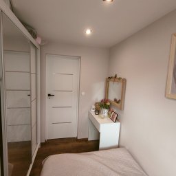 Tomasz Kubiak - Jasny pokój w Przybiernowie po remoncie, z łóżkiem w odcieniach różu, białą toaletką z lustrem ozdobionym kwiatami, przesuwną szafą z lustrami i białymi drzwiami z poziomymi panelami.