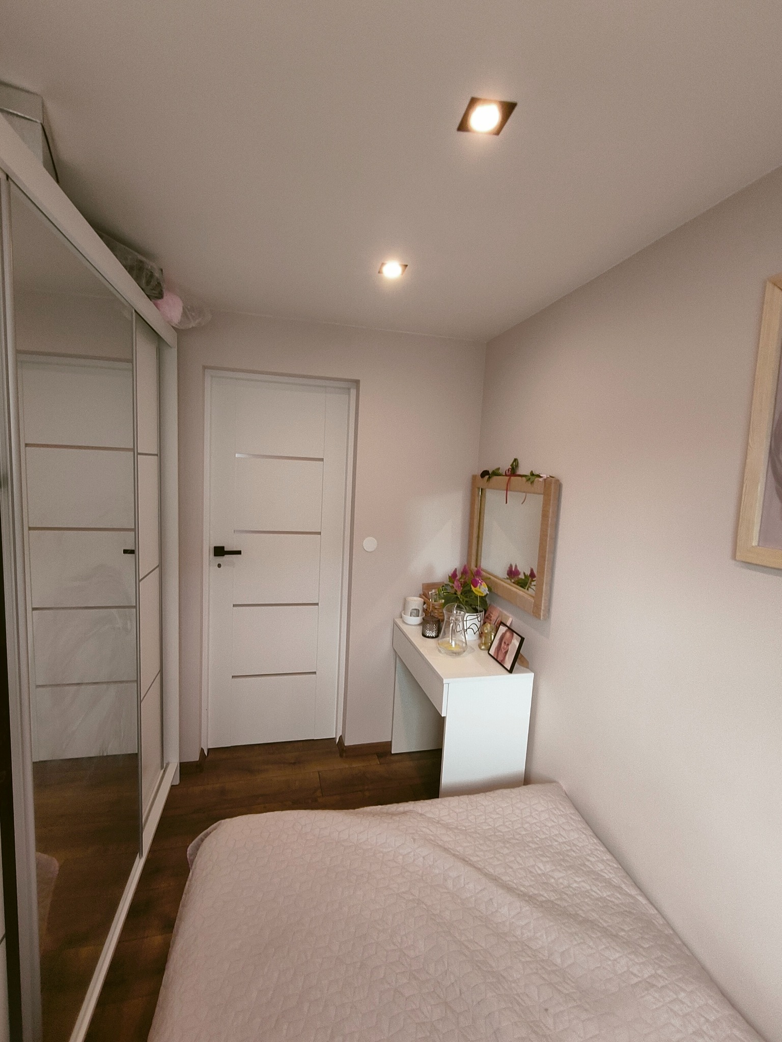 Jasny pokój w Przybiernowie po remoncie, z łóżkiem w odcieniach różu, białą toaletką z lustrem ozdobionym kwiatami, przesuwną szafą z lustrami i białymi drzwiami z poziomymi panelami.