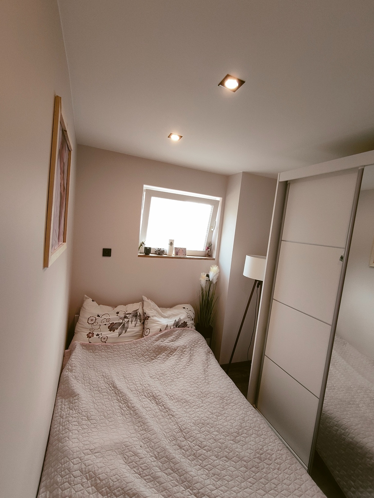 Niewielka sypialnia w odcieniach beżu z łóżkiem przy ścianie, przesuwną szafą z lustrem i oknem dachowym z widokiem na niebo.