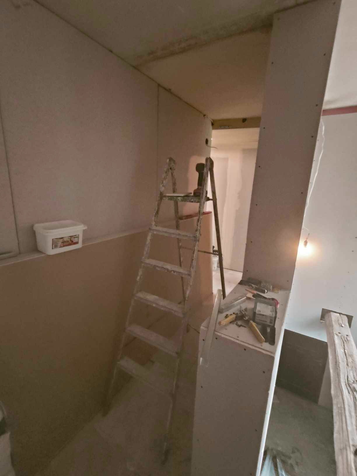 Poddasze w trakcie wykańczania płytami gipsowo-kartonowymi, widoczna drabina, narzędzia i wiadro z masą szpachlową.