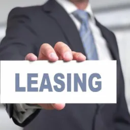 Mężczyzna w garniturze trzymający białą kartkę z napisem LEASING na rozmytym tle biurowym.