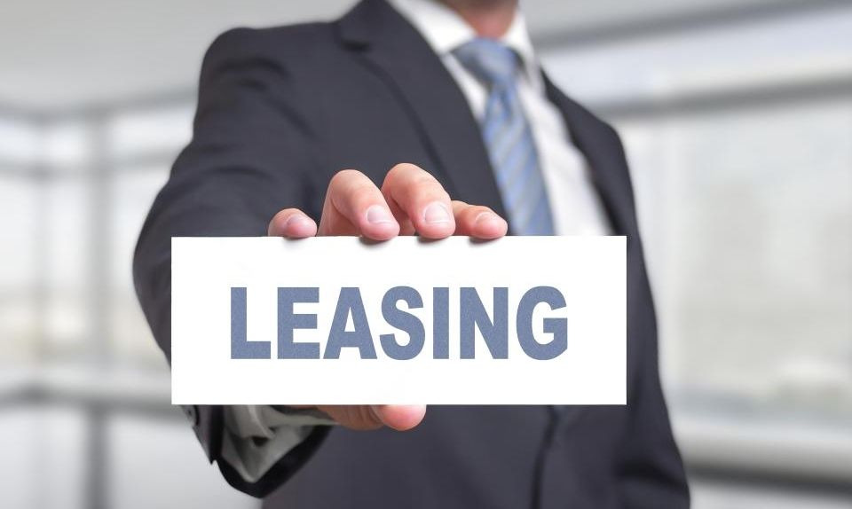 Mężczyzna w garniturze trzymający białą kartkę z napisem LEASING na rozmytym tle biurowym.