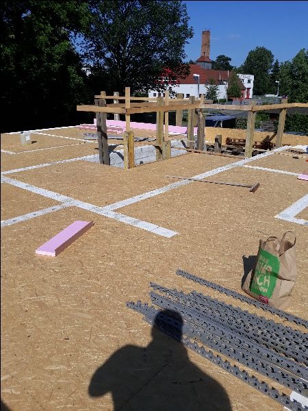 Wznoszenie konstrukcji domu murowanego: widok z góry na fundamenty, bloczki, drewniane podpory, izolację styropianową i materiały budowlane na placu budowy w słoneczny dzień.