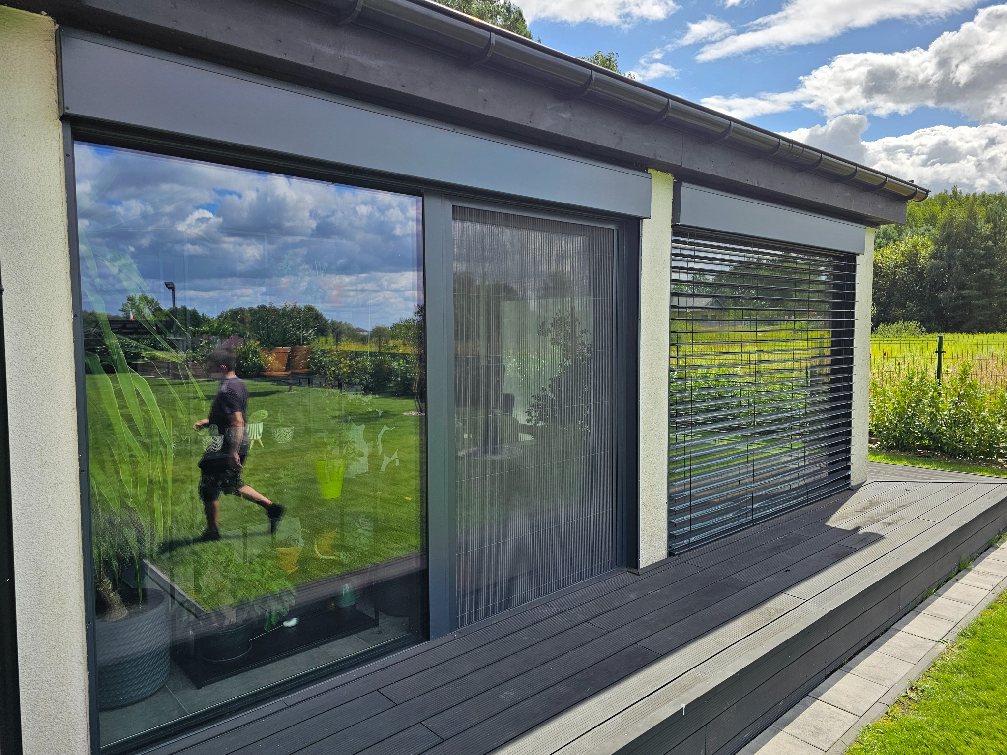 Nowoczesny dom z zamontowanymi roletami zewnętrznymi, moskitierą przesuwną i żaluzjami aluminiowymi w kolorze antracytowym, widok z zewnątrz na taras.