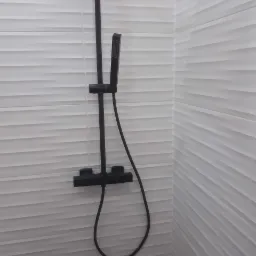 Czarny zestaw prysznicowy z deszczownicą na białych, poziomych płytkach o falistej strukturze.