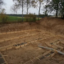 Przygotowanie szalunków pod fundament domu jednorodzinnego na działce z widokiem na łąkę i las.