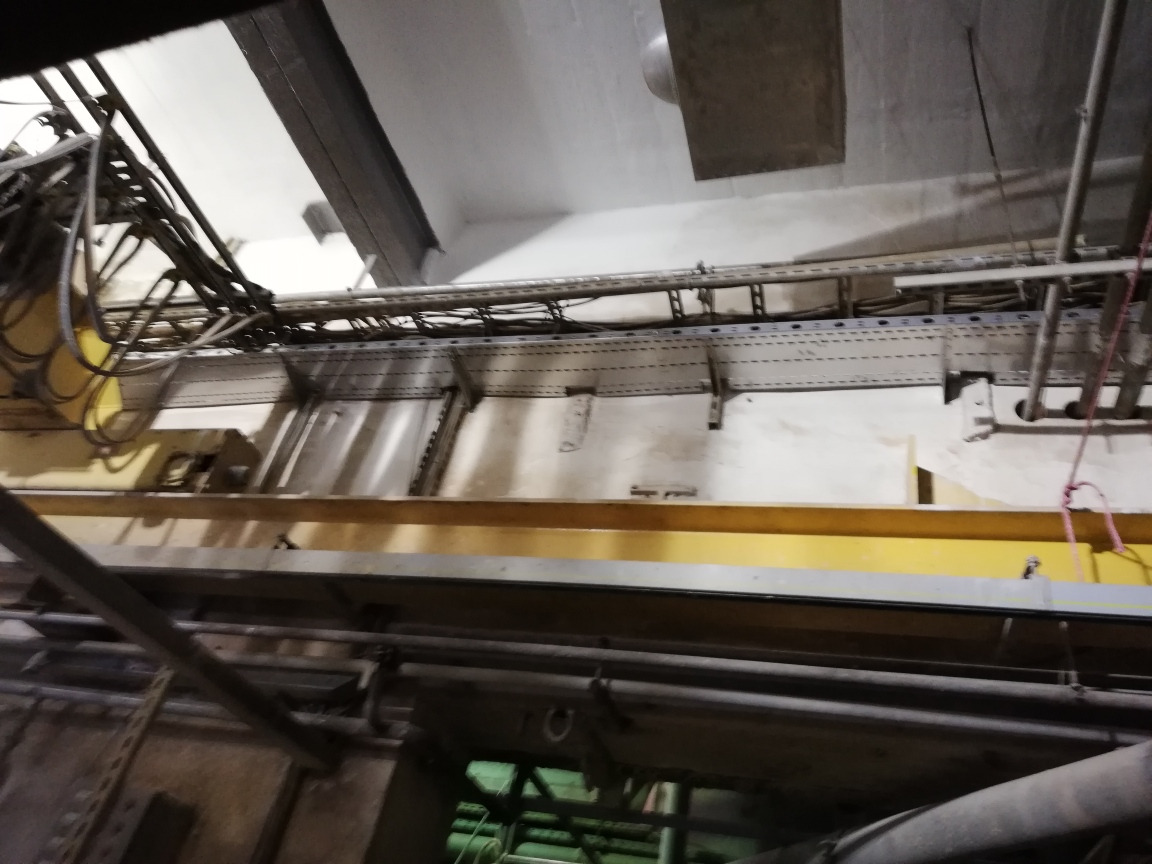 Widok z dołu na sufit techniczny z licznymi przewodami, rurami i korytkami kablowymi, zamontowanymi na metalowej konstrukcji, w pomieszczeniu o surowym wykończeniu.